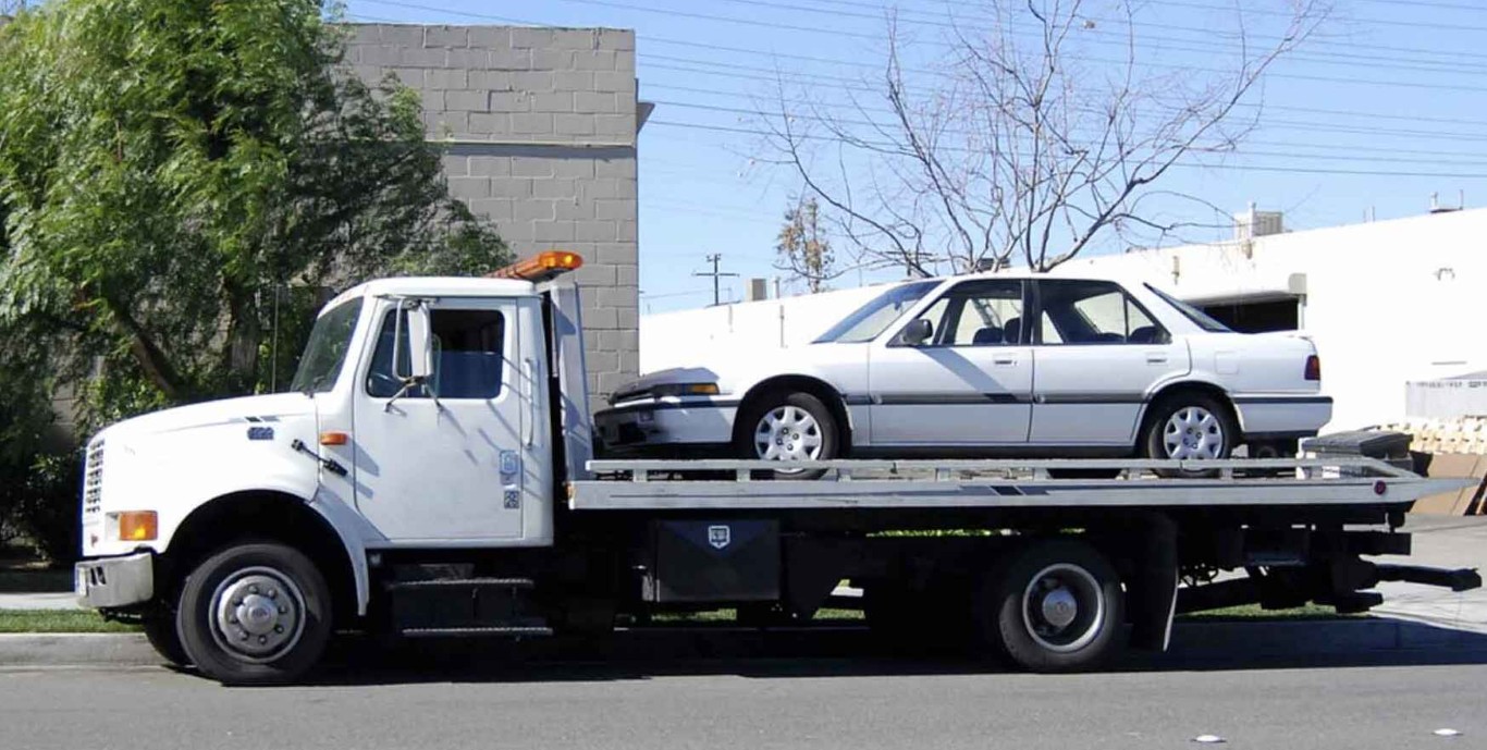 Tow truck technician providing flat tire change service on a city street